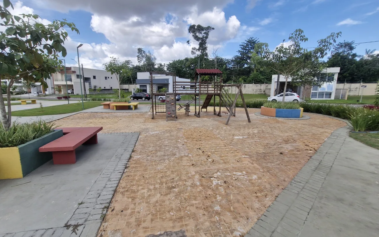 Área de lazer do condomínio antes da reforma, com piso de terra batida e playground de madeira desgastado